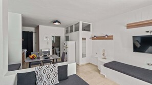 A compact living space with a kitchenette, dining area, and a TV mounted on the wall.