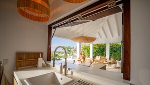 Una cocina moderna con un lavamanos grande, estantes de madera y vistas a un área de estar exterior.