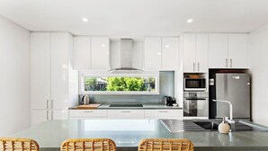 Cocina moderna con gabinetes blancos, una isla grande con asientos, electrodomésticos de acero inoxidable y vistas al exterior.
