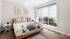 Un dormitorio con una cama, una mesita de noche, una ventana y dos cuadros en la pared.