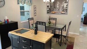 Ett modernt kök med matplats, med ett bord med glasskiva, svarta skåp och ett konstverk som föreställer en stadsbild på väggen.