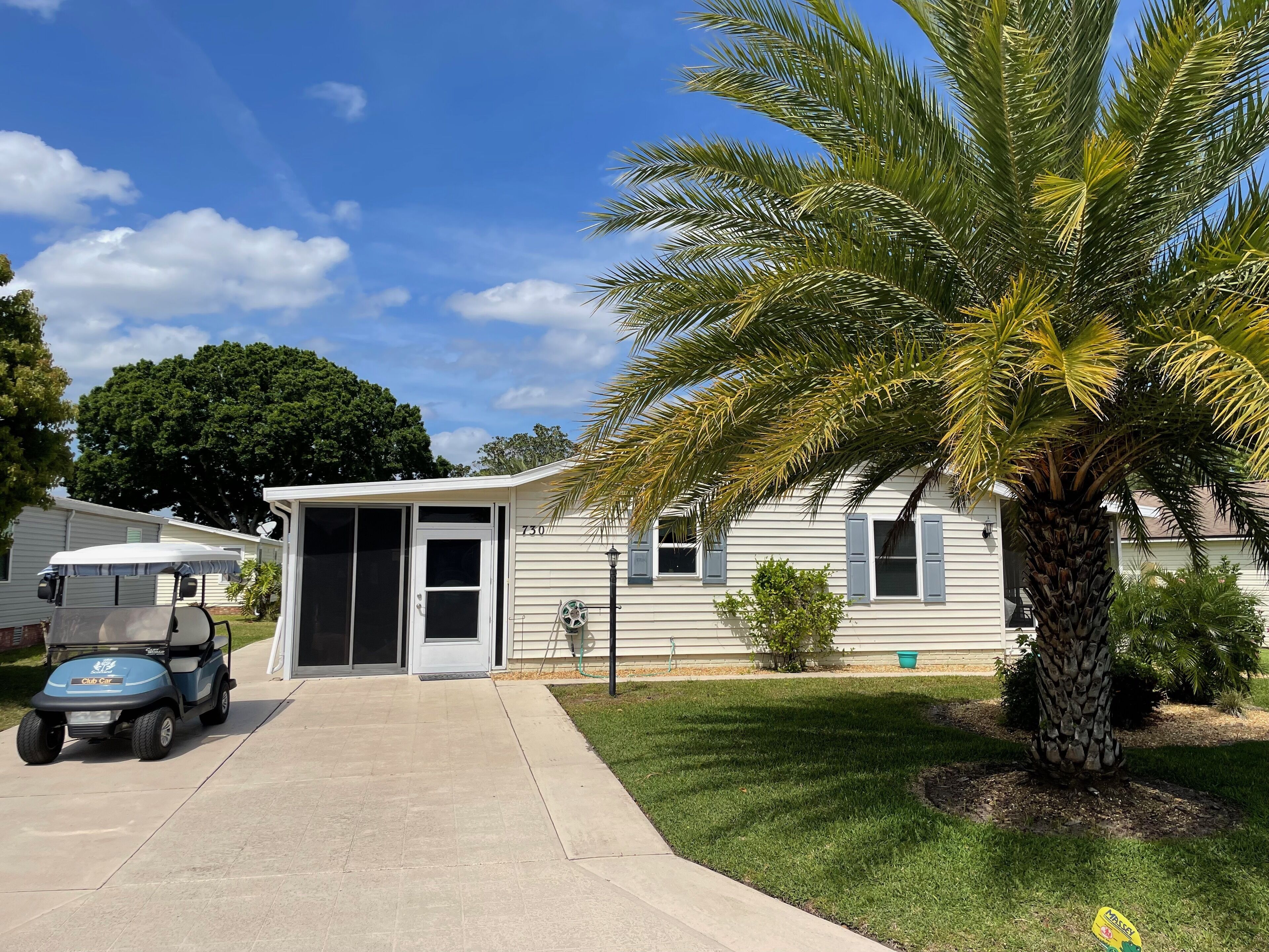 A single-story house with a garage, a palm tree, and a golf cart parked in front.