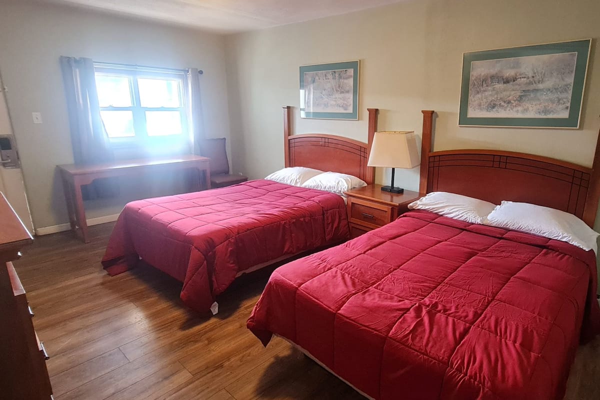 Ein Schlafzimmer mit zwei Betten, Holzboden, einem Schreibtisch und einem Fenster.