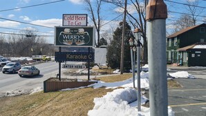 Et motel-skilt med teksten 'Kold øl to go' og branding for 'WERRY'S Motel & Pub', et skilt med 'Karaoke' og et piltavle, der viser 'ENTRÉ HER'.