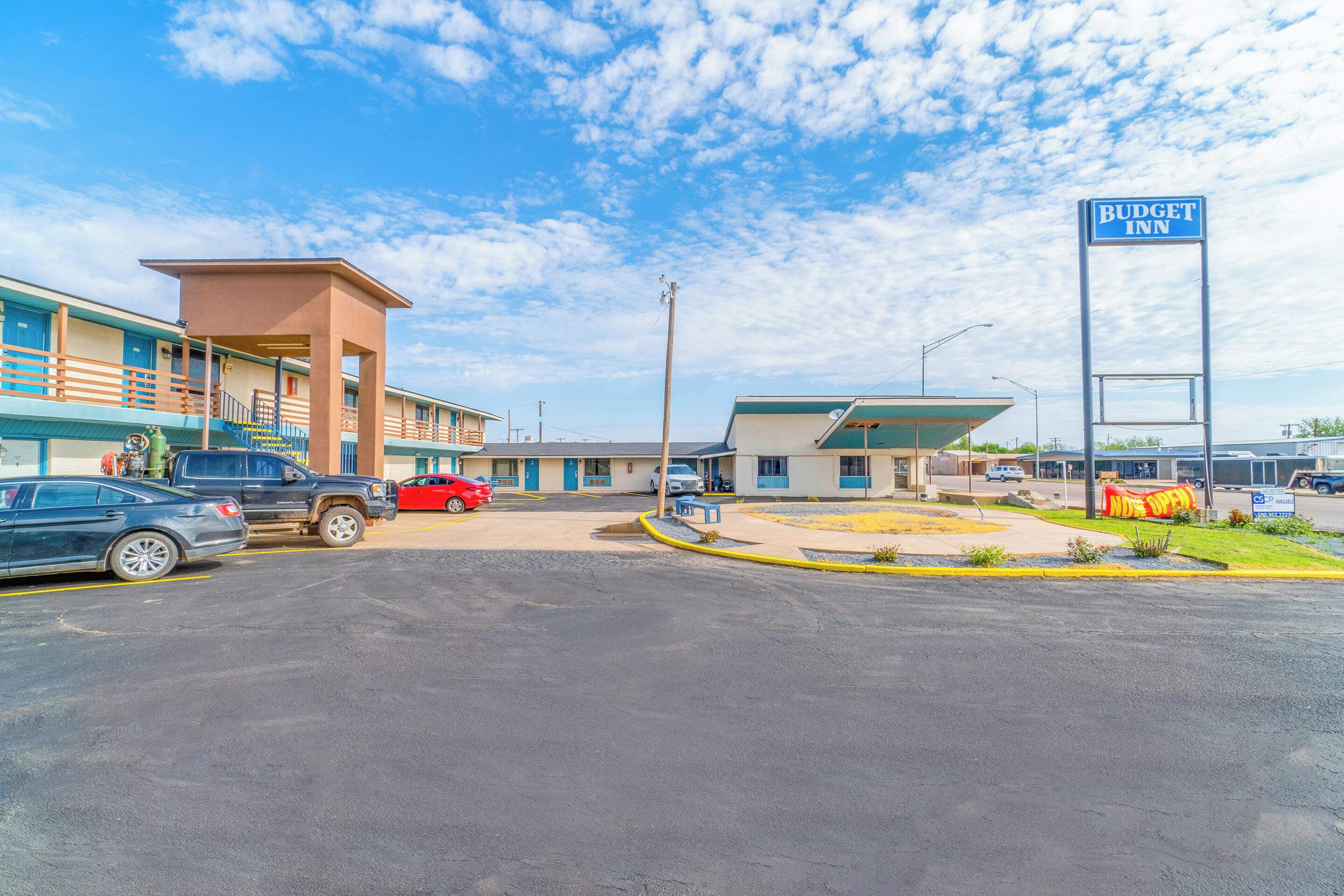 A motel with a blue sign, a parking lot, and a small garden area.