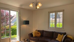 A living room with a brown leather sofa, a wooden coffee table, a floor lamp, and a view through a sliding glass door.