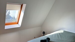 A bedroom with a single bed, a small bedside table, a lamp, and a skylight.