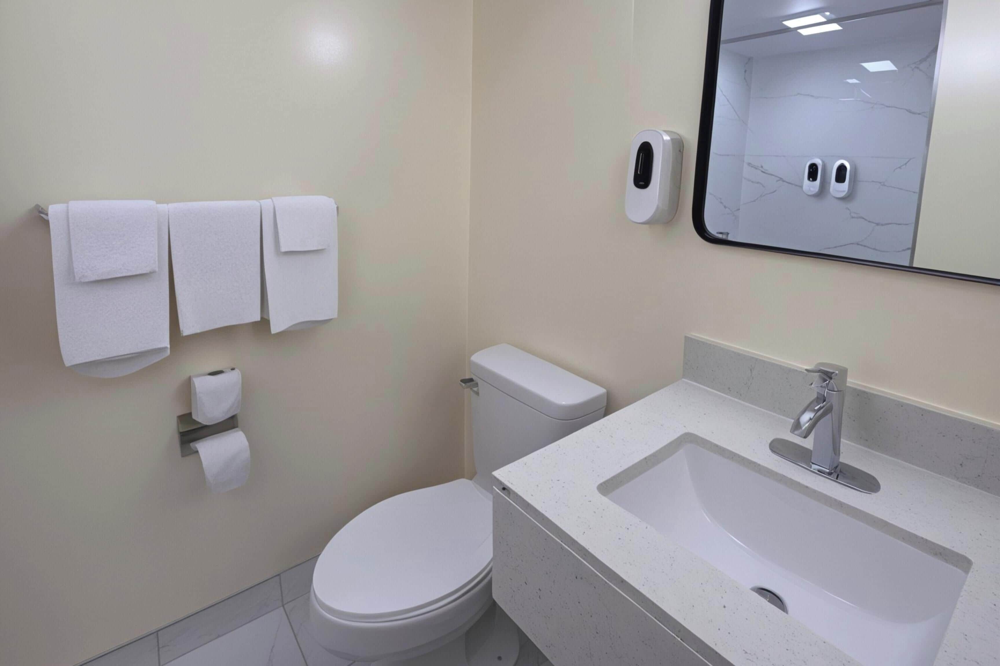 A bathroom with a toilet, sink, and towel dispenser.