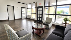 A spacious lobby with a dark wood floor, a round glass coffee table, a patterned armchair, a sofa, and large windows offering a view of the outside. - Washington Motel By Hotel O (Washington)