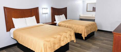 Una habitación de hotel con dos camas, una mesita de noche, un espejo y suelo de madera.