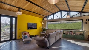 Een ruime woonkamer met een groot raam, een bank en een televisie aan de muur.