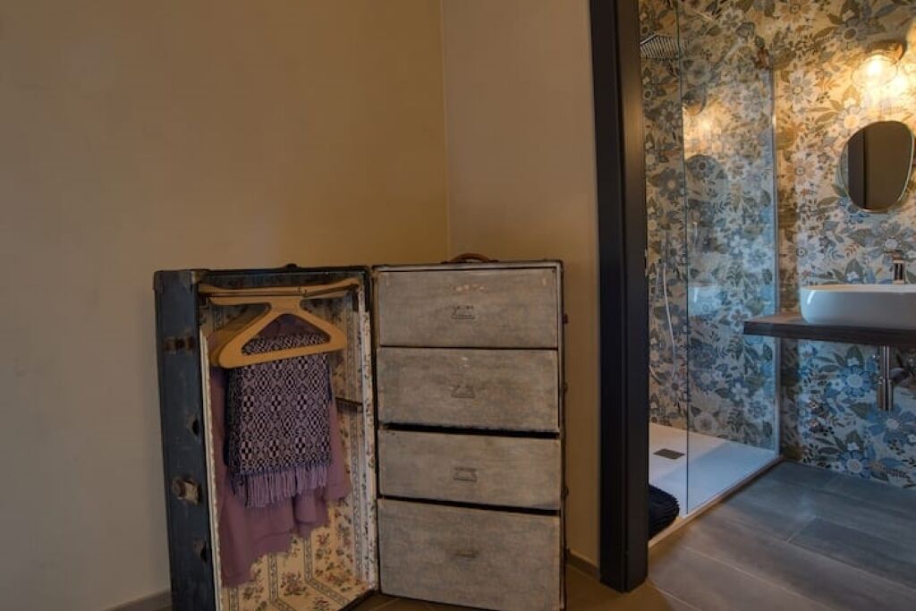 A bathroom with a floral wallpaper, a wooden cabinet with drawers, and a hanging garment.