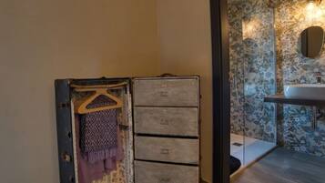 A bathroom with a floral wallpaper, a wooden cabinet with drawers, and a hanging garment.
