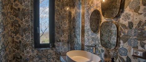 A bathroom with a large oval sink, a window, and floral patterned walls.