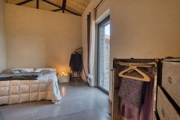 A bedroom with a bed, a hanging chair, a wardrobe, and a large window.
