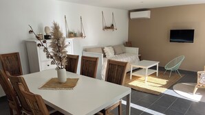 A modern living room with a white table, wooden chairs, a sofa, and a TV mounted on the wall. - Villa 60m² with garden, air conditioning and parking - up to 6 people (La Roquette-sur-Siagne)