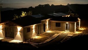 A row of small, single-story cabins with attached porches, illuminated by warm lighting, set against a backdrop of a clear sky and distant hills. - PaterMater b&b - Lana Room (Castell'Azzara)