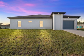 A single-story building with a garage, a small lawn, and a clear sky. - Serene Golf View Retreat 3 Bedroom Duplex by RedAwning (Lehigh Acres)