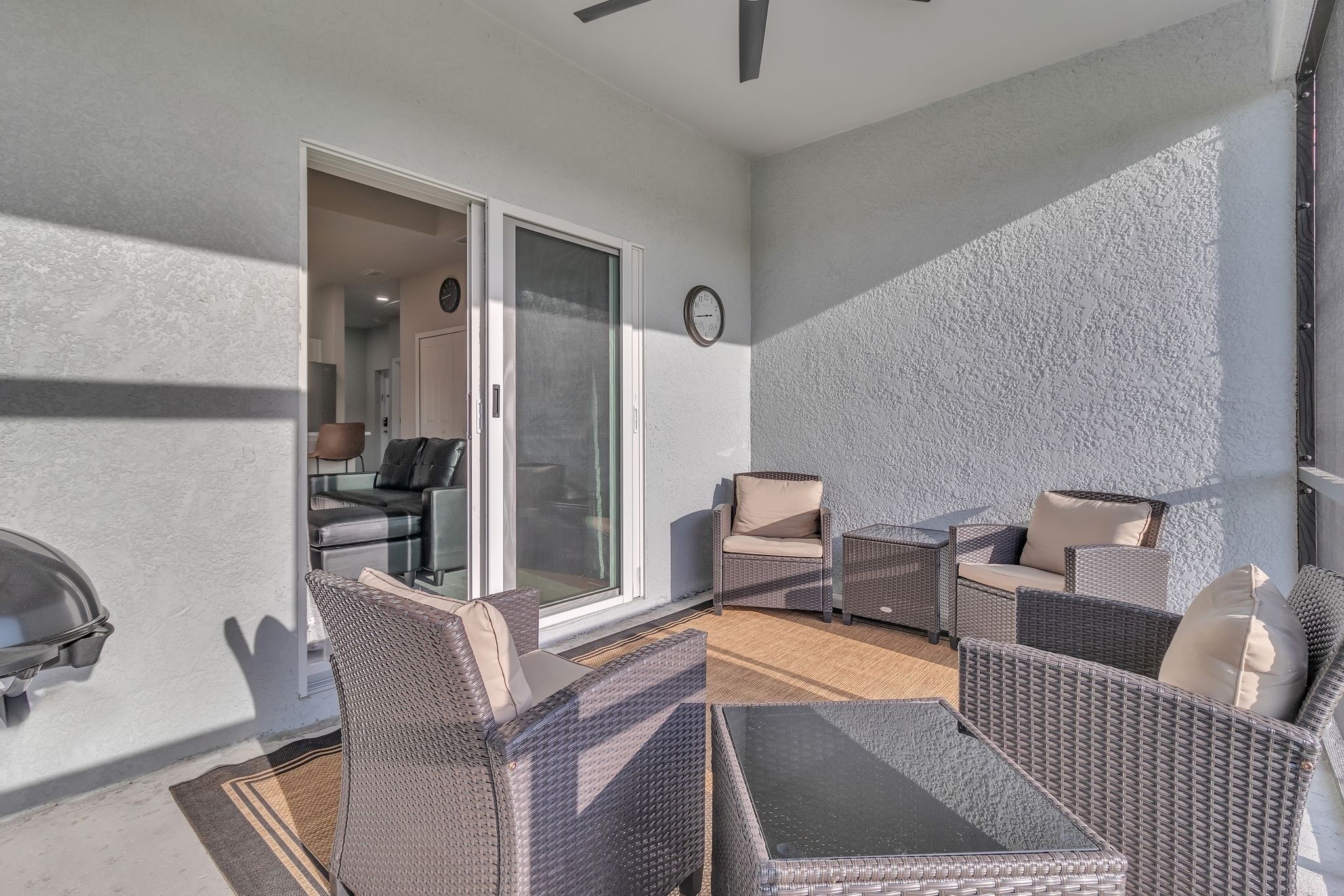 Une terrasse ensoleillée, meublée de meubles en osier, avec une porte-fenêtre coulissante et une horloge au mur.