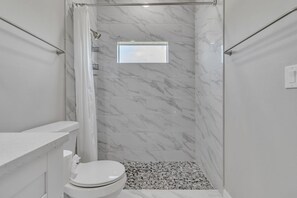 A bathroom with a shower, toilet, and a small window.