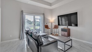A modern living room with a leather sofa, a glass coffee table, and a TV mounted on the wall. - Serene Golf View Retreat 3 Bedroom Duplex by RedAwning (Lehigh Acres)