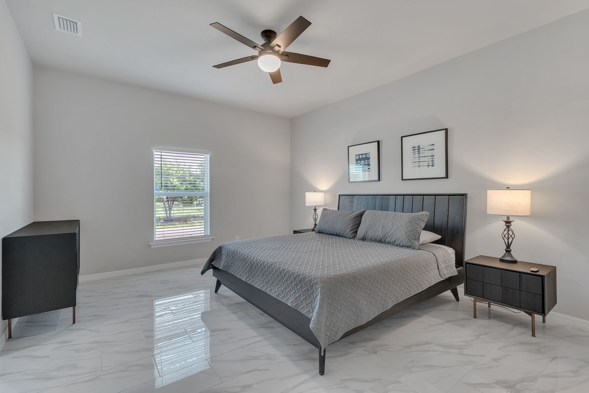 A bedroom with a bed, two bedside lamps, a ceiling fan, a window, and a dark cabinet.