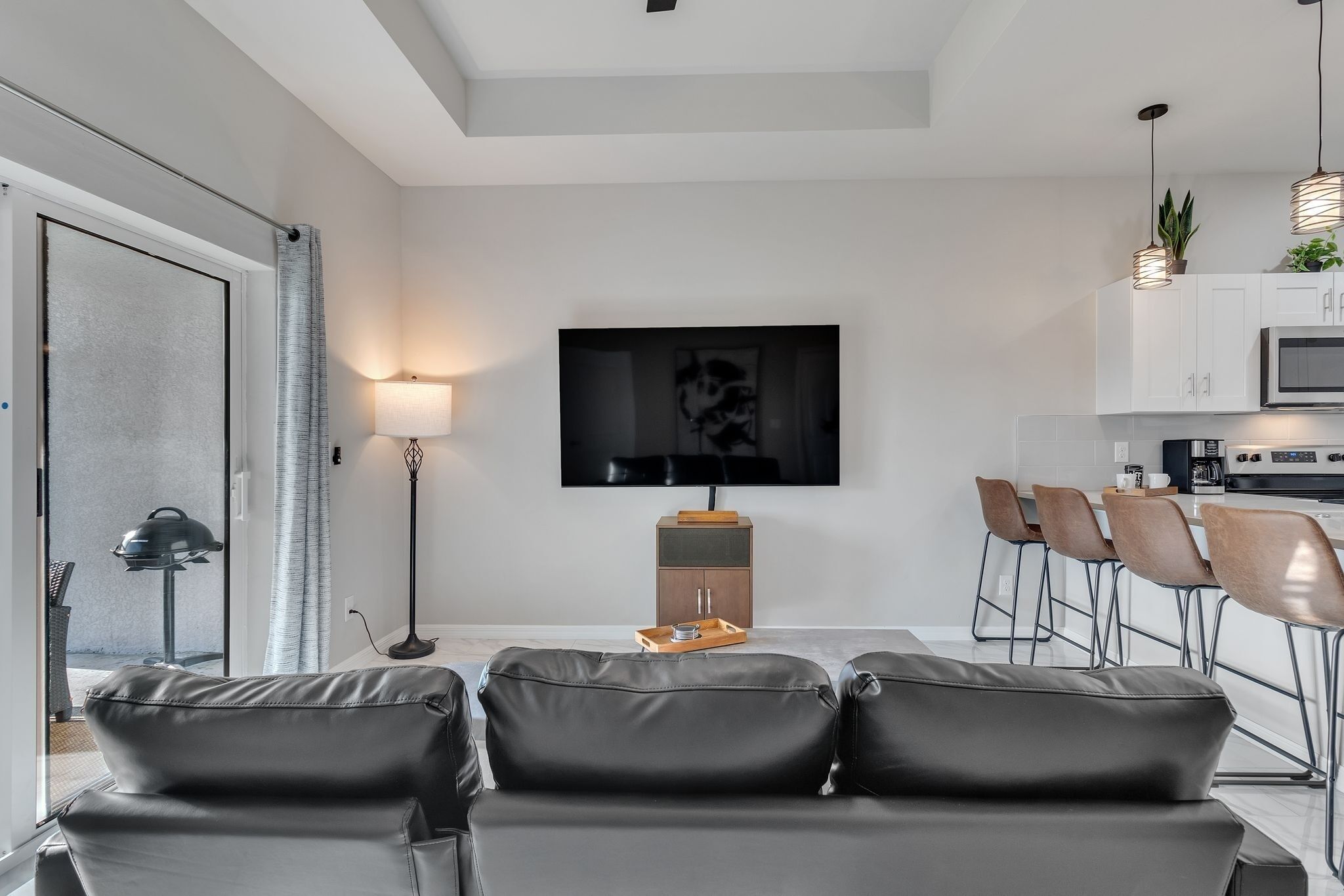 Een moderne woonkamer met een bank, een flatscreen-tv, een eethoek met stoelen en een keuken op de achtergrond.