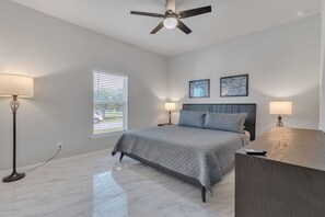 A bedroom with a bed, bedside lamps, a ceiling fan, and a window with blinds.