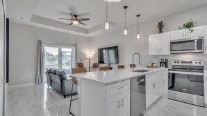 A modern kitchen with white cabinetry, a central island, stainless steel appliances, and pendant lighting. - Serene Golf View Retreat 3 Bedroom Duplex by RedAwning (Lehigh Acres)