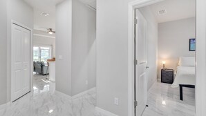 A hallway with a marble floor leading to a bedroom with a bed and nightstand. - Serene Golf View Retreat 3 Bedroom Duplex by RedAwning (Lehigh Acres)