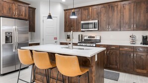 Une cuisine moderne avec des meubles en bois, des appareils en acier inoxydable et un îlot central doté de tabourets de bar.