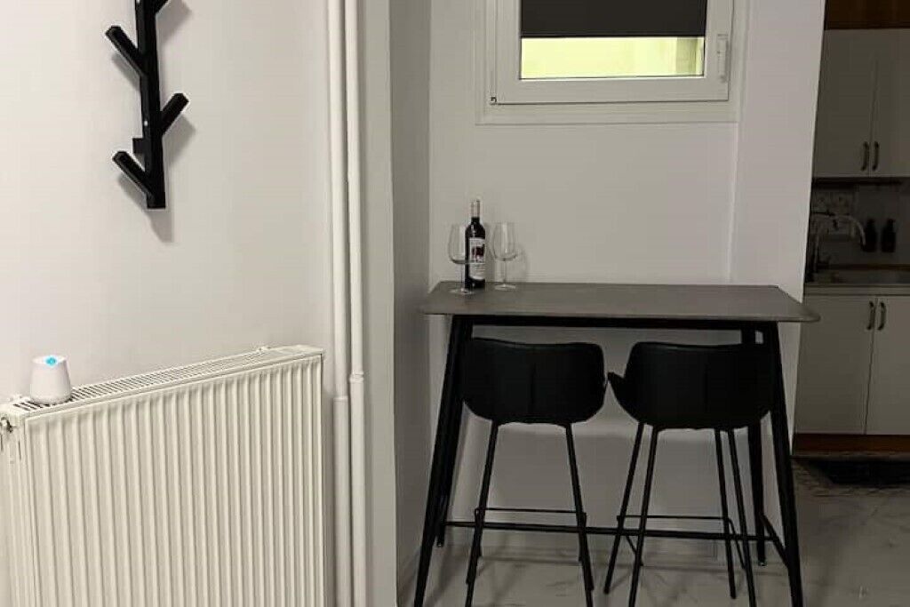 Een kleine keuken met een wit aanrecht, twee zwarte barkrukken, en een raam boven de spoelbak.