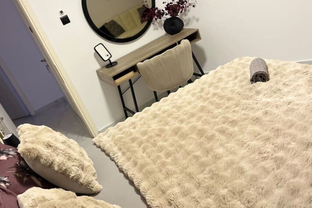 Un dormitorio con un tapete beige mullido, un espejo redondo, un escritorio de madera y una silla.