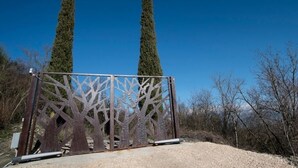 Ein Metallgitter mit Baumdekor, zwei hohe Bäume im Hintergrund und ein klarer, blauer Himmel.