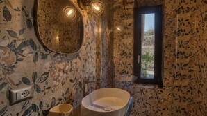 Ein Badezimmer mit einem großen, ovalen Waschbecken, einem runden Spiegel und einem Fenster mit Blick auf Grünflächen.