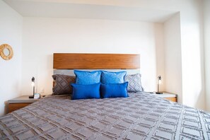 A neatly made bed with a patterned bedspread and two nightstands with lamps. - Top-Floor 2BR w/ Skyline Views, Pool & Gym (Puerto Vallarta)