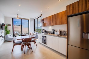 A modern kitchen with a dining area, wooden cabinets, and a view of the city. - Top-Floor 2BR w/ Skyline Views, Pool & Gym (Puerto Vallarta)
