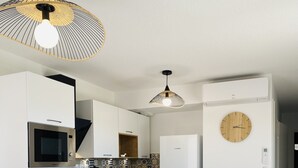 A modern kitchen with white cabinets, stainless steel appliances, a wooden dining table with chairs, and a wall clock. - Appart 4 Pers Climatisé Avec Terrasse, Parking et Piscine Collective - V0816 (Vias)