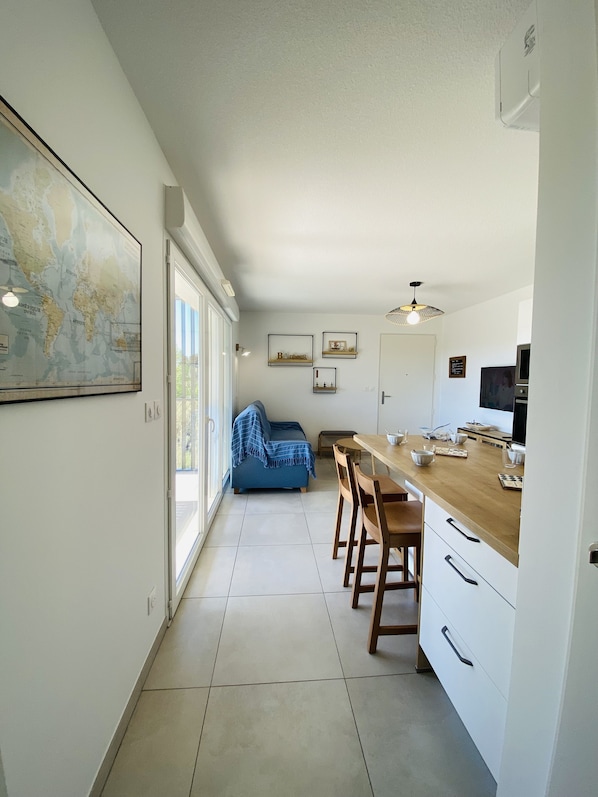 Una cocina moderna con encimera de madera, armarios blancos y una zona de comedor con sillas.