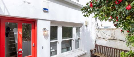 Um prédio branco com uma porta vermelha, janelas e um banco.
