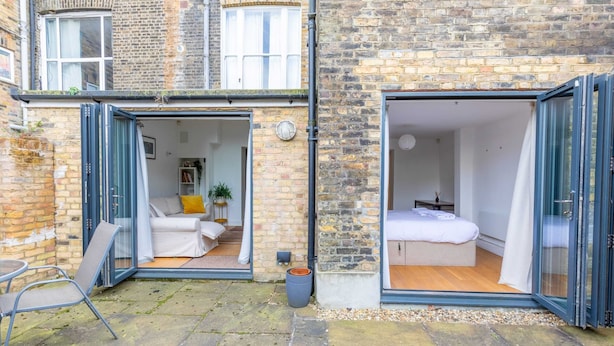 A two-bedroom apartment with an open-plan living area and a separate bedroom, featuring a brick exterior and a small outdoor seating area. - Homely 2BD Flat W/private Patio Near Maida Vale! (London)