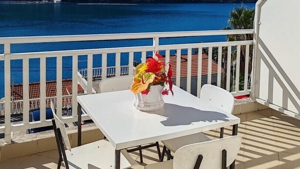 A terrace with a white table and chairs, a vase of flowers, and a view of a lake and hills.