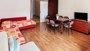 A compact living space with a sofa, a dining table with chairs, a TV, and a wardrobe.