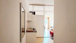 A narrow hallway with a kitchenette area featuring a refrigerator, microwave, and small countertop.
