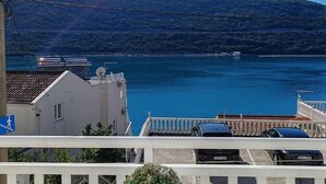 A balcony with a potted plant, overlooking a body of water and a hilly landscape.