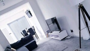 A modern living room with a black sofa, a white coffee table, a large rug, and a tripod. - Beautiful 3-bed House in Birmingham (Birmingham)