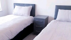 Two single beds with white linens and dark headboards in a room with a window and a small bedside table. - Beautiful 3-bed House in Birmingham (Birmingham)