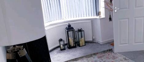 A room with a large window, a standing lamp, a patterned rug, and a door.