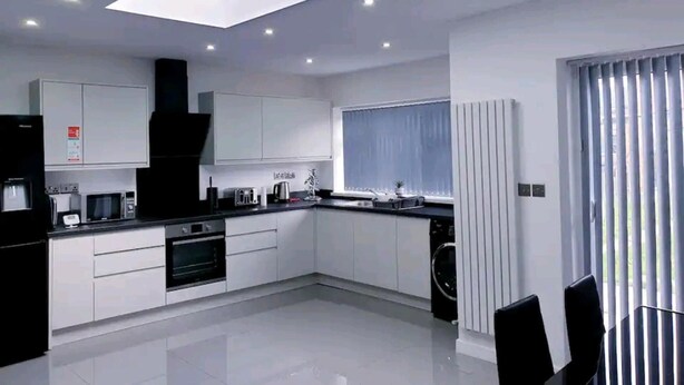 A modern kitchen with white cabinets, a black countertop, a built-in oven, and a skylight. - Beautiful 3-bed House in Birmingham (Birmingham)