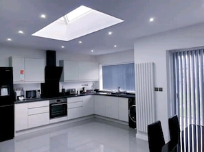 A modern kitchen with white cabinets, a black countertop, a built-in oven, and a skylight. - Beautiful 3-bed House in Birmingham (Birmingham)